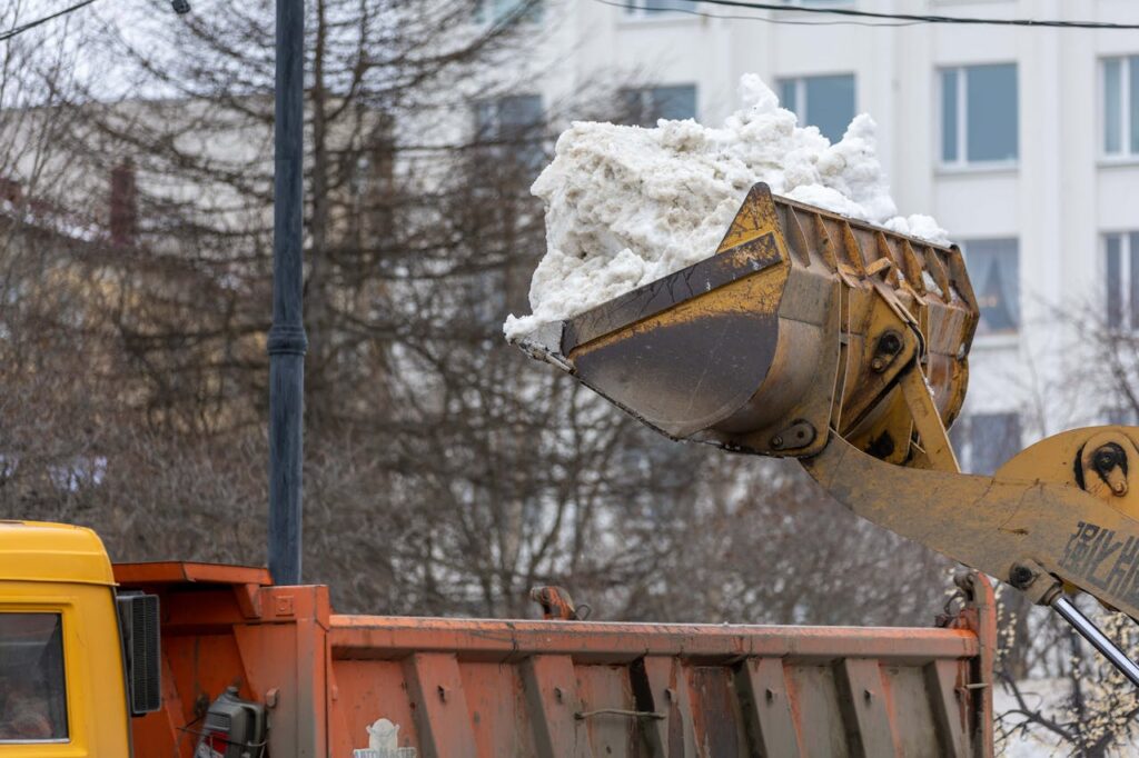 pexels photo 27306406 Excavator clearing snow into dump truck on city street during winter.